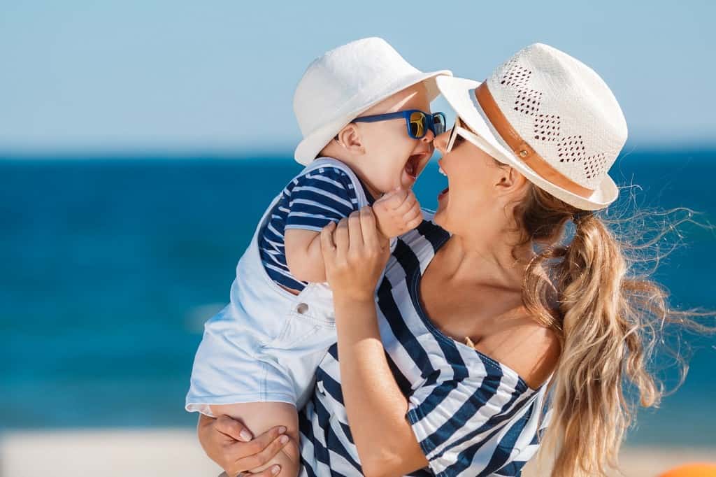 Young mother and her young son on the beach. a person wearing a hat and sunglasses
