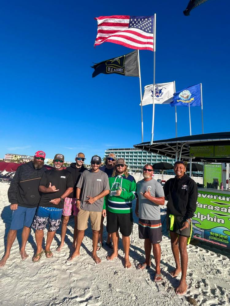 Group of people standing on a beach in front of flags and a building.