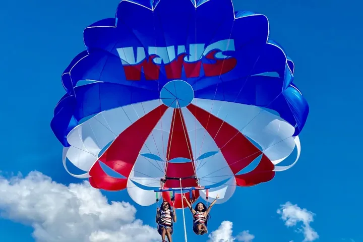 Two people parasailing with a red, white, and blue parachute against a blue sky.