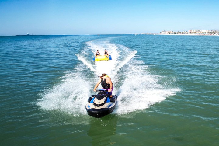 Person on jet ski towing inflatable banana boat with two riders on the ocean.