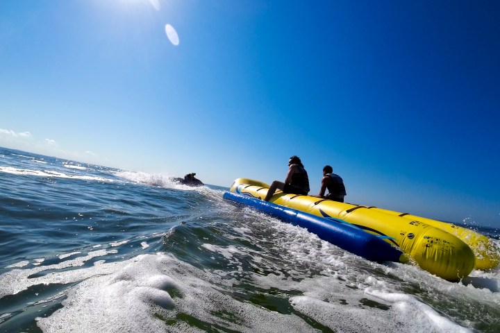 Two people riding a yellow banana boat on the ocean with clear blue skies.