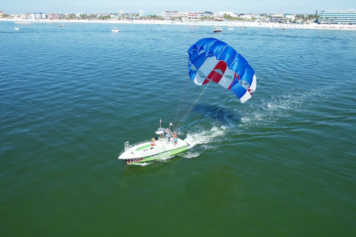 Boat with parasail on ocean, beach and buildings in background.