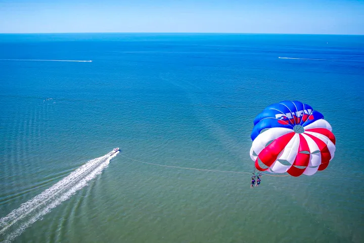 Parasailing over blue ocean with a boat pulling red, white, and blue parachute.