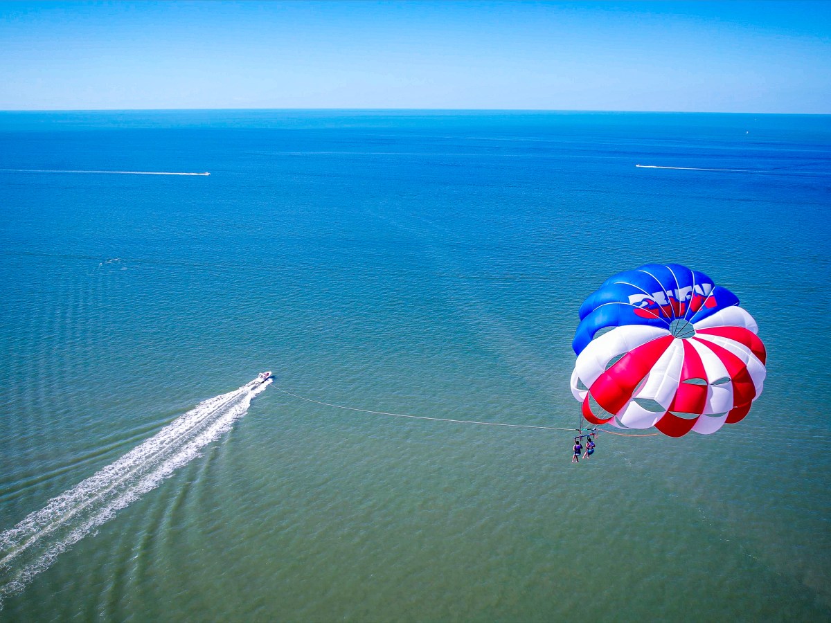Parasailing over blue ocean with a boat pulling red, white, and blue parachute.